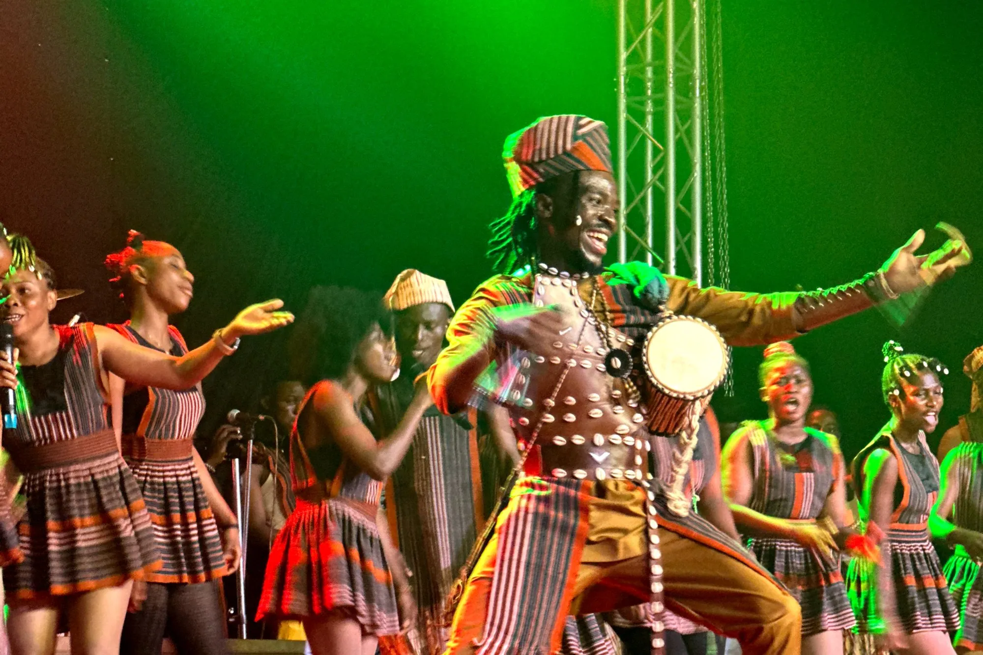 The Abuletic King dances with the talking drum among his company, under green stage light